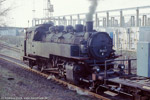 April 1985. 86 607. Zwickau / 86 607 hat mit einer auf einem Flachwagen verladenen Maschine fast den höchsten Punkt der Brückenbergbahn erreicht. Im Hintergrund ist das Betonplattenwerk zu erkennen. Hier wurden die Wandelemente der Plattenbauten vorgefertigt und per LKW zu den Baustellen, unter anderem nach Zwickau-Eckersbach und Werdau transportiert. Auf Grund des rapiden Bevölkerungsrückgangs nach der Wiedervereinigung wurden viele der damals neu gebauten Häuser in der Zwischenzeit bereits wieder abgerissen.